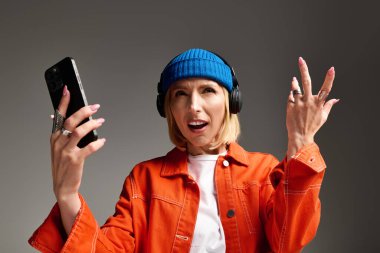 Şık, sarışın bir kadın telefonuyla oynuyor, modern bir stüdyoda müzik dinliyor..