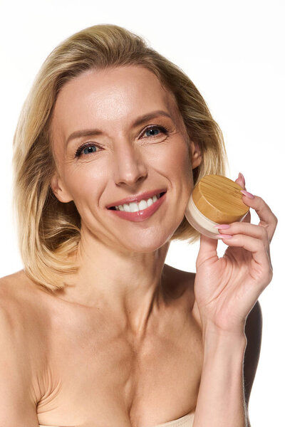 Красивая блондинка демонстрирует свою страсть к уходу за кожей, держа продукт.