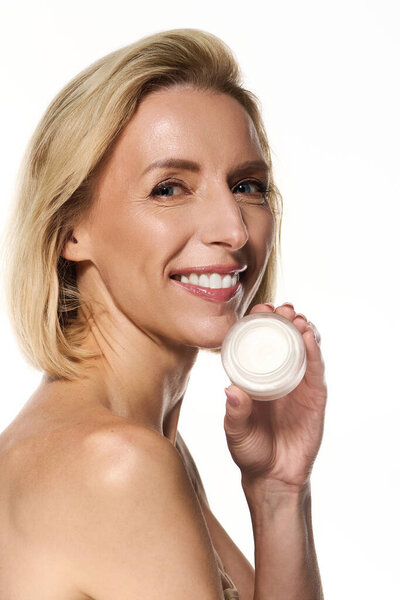 Блондинка держит продукт по уходу за кожей, продвигая его преимущества для здоровой, светящейся кожи.