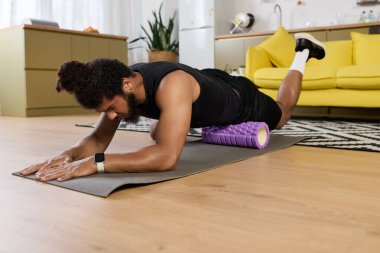 Atletik bir adam rahat bir yaşam alanında köpük bir silindirle esneme ve iyileşme pratiği yapar..