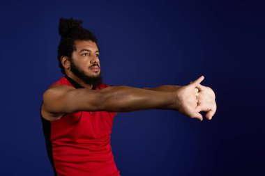 Kıvırcık saçlı ve sakallı genç bir sporcu mavi arka planda egzersiz yapıyor..