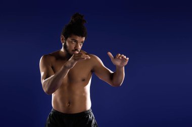 Kıvırcık saçlı ve sakallı atletik adam mavi arka planda çeşitli egzersizler yapıyor..