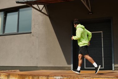 Sakallı enerjik bir adam canlı yeşil kapüşonlu bir kapüşonluyla dışarı koşuyor..