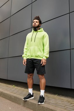 Yeşil kapüşonlu Afro-Amerikan bir adam dışarıda spor yapıyor, atletizmini sergiliyor..