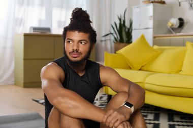 Sakallı ve kıvırcık saçlı atletik bir adam evindeki oturma odasında sakince çalışıyor..