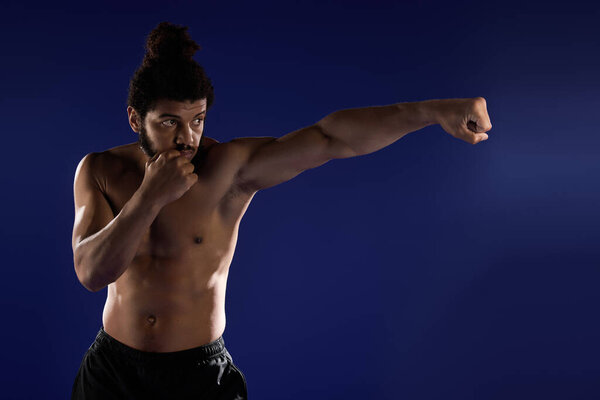 Атлетик фокусируется на своей тренировке, когда он тренируется с мощным ударом на синем фоне..