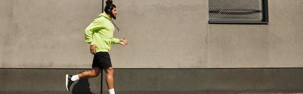 African American man exercises in a green hoodie, jogging along a city street, banner