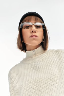 Bu şık genç bayan, gün ışığında kalın gözlükleri ve beresi olan şık bir giysinin modelliğini yapıyor..