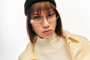 Moda kıyafetleri ve şık gözlükleri olan kendine güvenen genç bir kadın parlak bir ortamda duruyor..