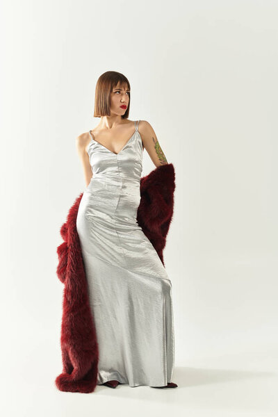 Confident young woman in a stunning silver dress and luxurious red shawl.