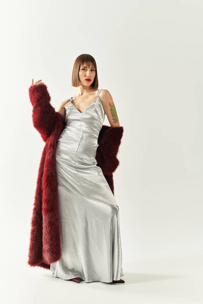 Fashionable young woman poses gracefully in a silver dress and cozy outerwear, exuding style.
