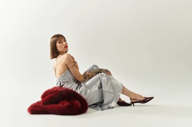 Kendine güvenen genç bir kadın zarif gümüş bir elbise içinde, çarpıcı bir görünüm sergiliyor..