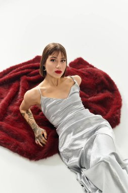 Kendine güveni tam genç bir kadın, yumuşak kırmızı bir battaniyeye sarılıp şık gümüş elbisesini öne çıkarıyor..