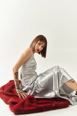 Şık bir genç kadın ışıldayan gümüş bir elbise içinde kendine güvenen bir poz verir..