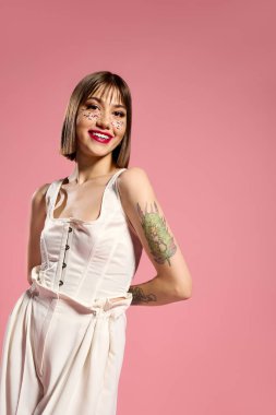 Güzel, genç bir kadın ışıl ışıl gülümser, çarpıcı dövmeleri olan şık kıyafetler giyer..