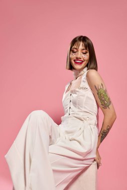 Beyaz elbiseli genç bir kadın dövmelerini ve canlı gülüşünü gösteriyor..