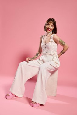 Tarz sahibi genç bir kadın, yumuşak pembe bir arka plana karşı şık bir şekilde poz verir..