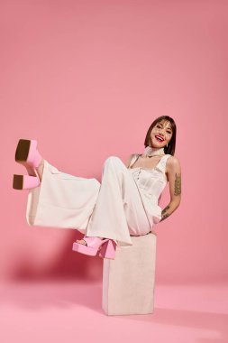 Moda kıyafetli genç bir kadın bir blokta otururken neşeli ruhunu sergiliyor..