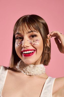 Genç bir kadın şık kıyafetlerini ve neşeli makyajını cazibeyle dolu canlı bir ortamda sergiliyor..