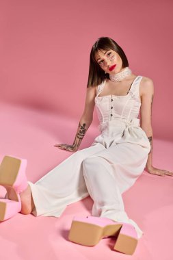 Kendine güvenen genç bir kadın pembe bir yüzey üzerinde şık kıyafetini sergiliyor..