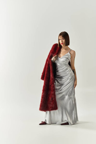 Confident young woman in a silver dress and red shawl in a stylish setting.