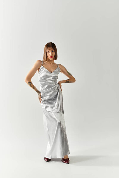 A stylish young woman stands confidently in a silver gown, embodying contemporary fashion trends.