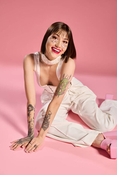 Молодая женщина в модной одежде улыбается на розовом фоне, подчеркивая свои татуировки.