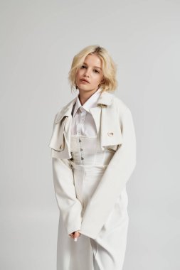 Genç sarışın bir kadın, modern modanın somutlaştırılmış gri stüdyosunda bir kış kıyafeti sergiliyor..