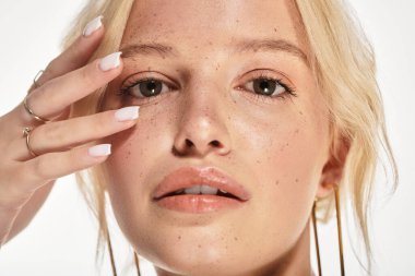 Genç sarışın bir kadın beyaz bir stüdyo ortamında zarifçe poz veriyor..