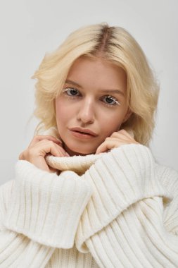 Beyaz kirpikli genç sarışın bir kadın rahat örülmüş bir süveter içinde poz veriyor..