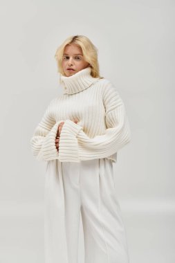 Genç sarışın bir kadın zarif bir şekilde örülmüş bir kazakla poz veriyor, kışın cazibesini yakalıyor..