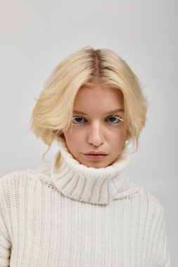 Samimi bir süveter giyen kendine güvenen genç bir sarışın stüdyoda eşsiz beyaz kirpiklerini ön plana çıkarıyor..