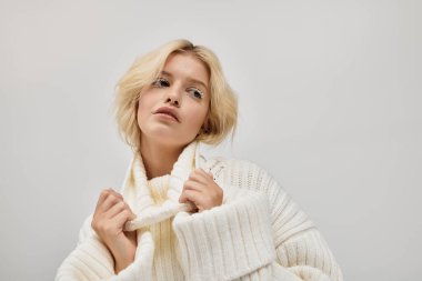 Sarışın genç bir kadın, stüdyoda kışın gösteriş yapan rahat örgü bir süveter mankenliği yapıyor..