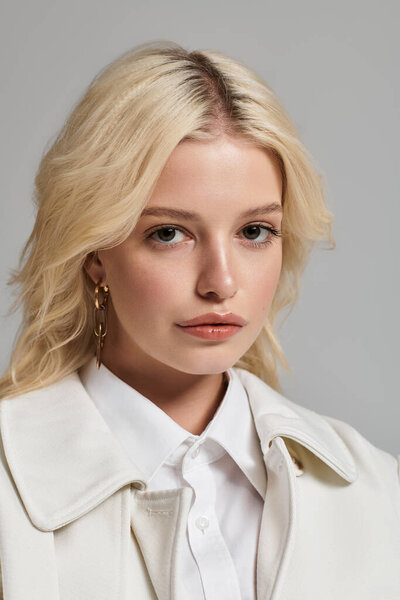 Милая молодая блондинка демонстрирует свой модный зимний наряд в серой студии.