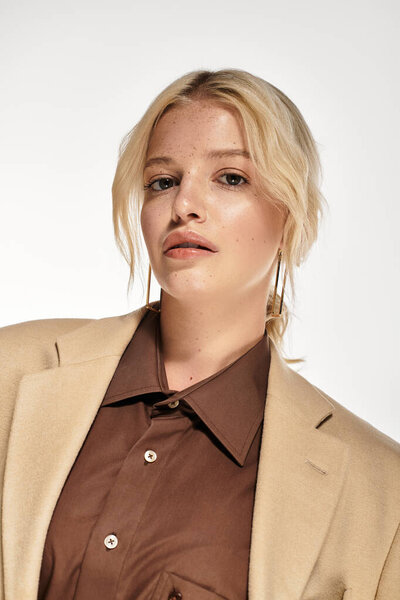 Молодая блондинка уверенно позирует в модном зимнем наряде на ярком белом фоне.