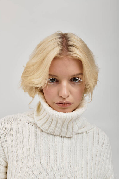 Уверенная молодая блондинка в уютном свитере подчеркивает свои уникальные белые ресницы в студии.