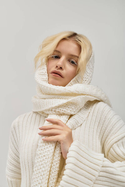 A beautiful young blonde woman poses warmly in a cozy knitted sweater, exuding winter charm.