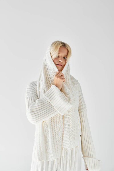 Молодая блондинка изящно позирует в уютном трикотажном свитере, источая тепло и красоту.