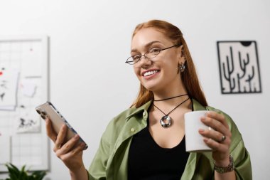 Genç bir kadın evinde vakit geçirmekten zevk alıyor, bir kupadan yudumluyor ve telefonunu kullanırken neşeli görünüyor..