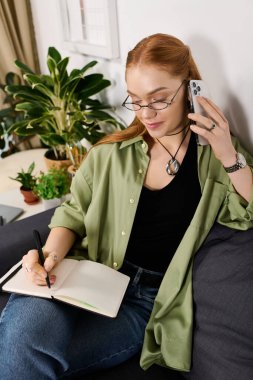 Genç bir kadın evinde dinleniyor, telefonda konuşurken rahat bir kanepeye not defterini yazıyor..
