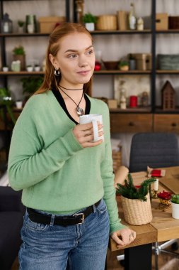 Genç bir kadın, sıcak bir fincan tutarak evinde dinleniyor. Sıcak bir atmosfer ve dekorasyonla çevrili..