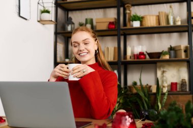 Kırmızı kazaklı genç bir kadın evinde içkiyle gülümsüyor..