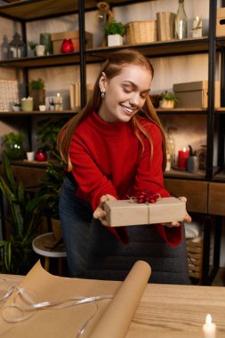 Genç bir kadın evinde hoş bir hediyeyi sıcacık bir atmosferde sararken ışıl ışıl gülümser..