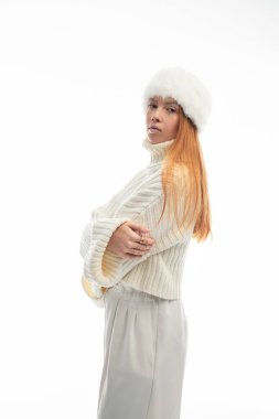 Genç kızıl saçlı bir kadın, rahat bir süveter ve kürk şapkayla, kış tarzını yakalıyor..