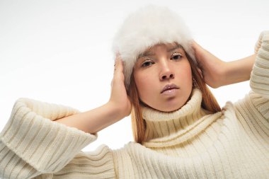 Kızıl saçlı genç bir kadın kendine güvenerek poz veriyor. Şık bir kış elbisesi ve kürk şapkası var..