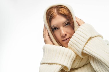 Süveter giymiş genç bir kadın parlak beyaz bir arkaplanda poz veriyor, kış tarzını gösteriyor..