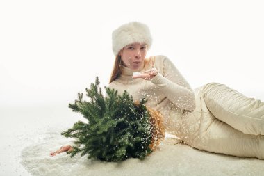 Sıcak süveter ve kürk şapkalı kızıl saçlı kadın küçük bir Noel ağacıyla şakalaşıyor..