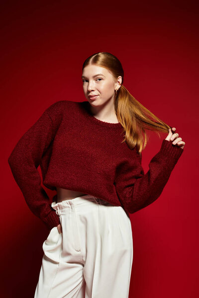 Молодая женщина с яркими рыжими волосами уверенно позирует в уютном зимнем свитере, излучающем стиль.