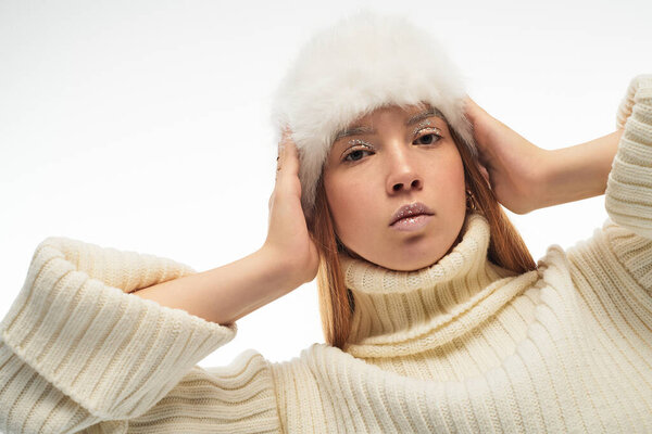 Молодая женщина с рыжими волосами уверенно позирует в стильном зимнем наряде с меховой шляпой.