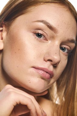 Kızıl saçlı ve çilli genç bir kadın zarif bir şekilde poz veriyor, güzelliğini gösteriyor..